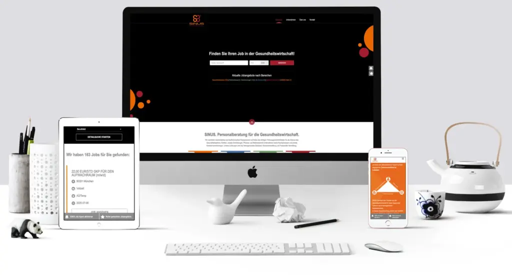 Ein minimalistischer Arbeitsplatz mit Desktop-Computer, Tablet und Smartphone, auf dem eine Website angezeigt wird. Der Schreibtisch verfügt über eine weiße Tastatur, eine Maus, eine Pandafigur und eine Teekanne. Die Farbgebung ist Schwarz, Weiß und Orange.