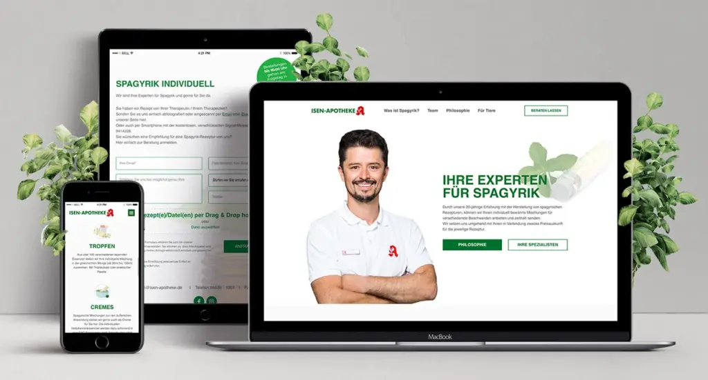 Auf Desktop-PCs, Tablets und Smartphones wird die Website einer Apotheke angezeigt, auf der ein bärtiger Mann im weißen Hemd mit verschränkten Armen abgebildet ist. Grüne Blättergrafiken umgeben die Geräte. Der Text auf den Bildschirmen ist auf Deutsch und wirbt für Fachwissen zu spagyrischen Heilmitteln.